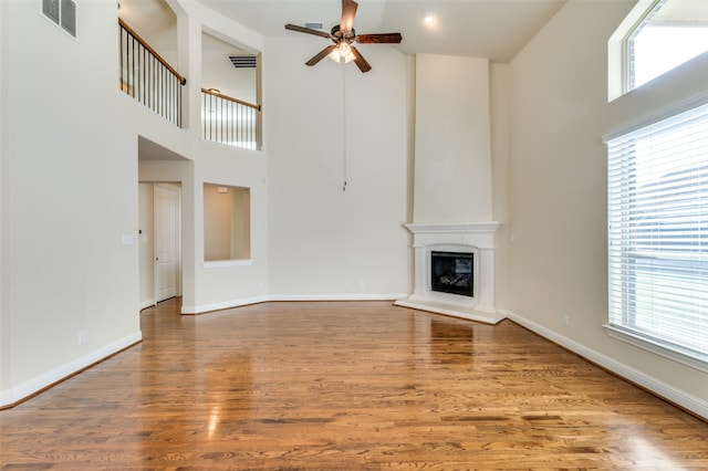 unfurnished living room featuring a high ceiling, ceiling fan, and hardwood / wood-style flooring