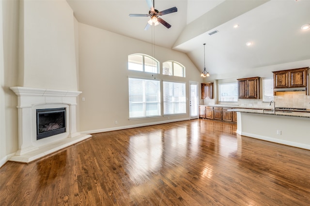 unfurnished living room featuring ceiling fan with notable chandelier, hardwood / wood-style flooring, sink, and high vaulted ceiling