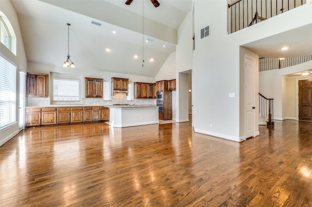 kitchen with decorative backsplash, high vaulted ceiling, ceiling fan with notable chandelier, wood-type flooring, and a center island