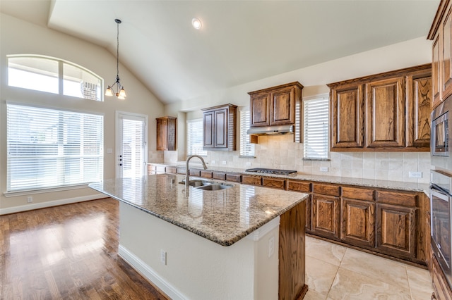 kitchen featuring backsplash, decorative light fixtures, light hardwood / wood-style flooring, sink, and a center island with sink