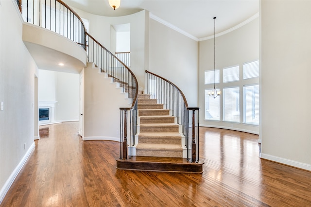 stairs with a towering ceiling, crown molding, and wood-type flooring