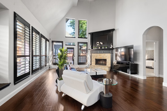 living room featuring high vaulted ceiling, dark wood-type flooring, and a stone fireplace