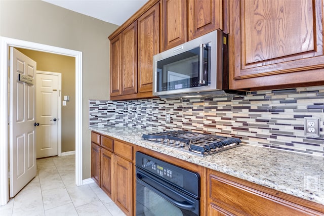 kitchen with light stone countertops, light tile patterned flooring, appliances with stainless steel finishes, and backsplash