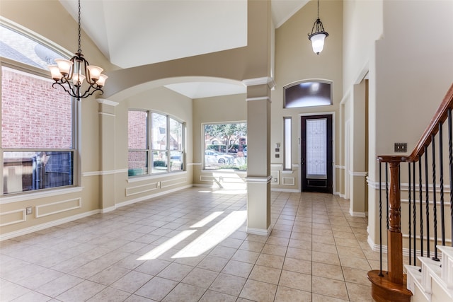 tiled foyer featuring high vaulted ceiling, a notable chandelier, and ornate columns