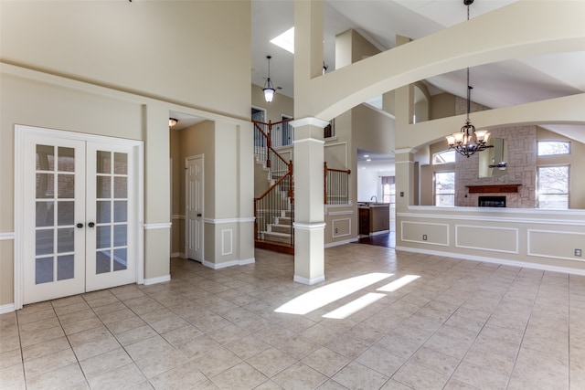 unfurnished living room with light tile patterned floors, french doors, high vaulted ceiling, a notable chandelier, and ornate columns