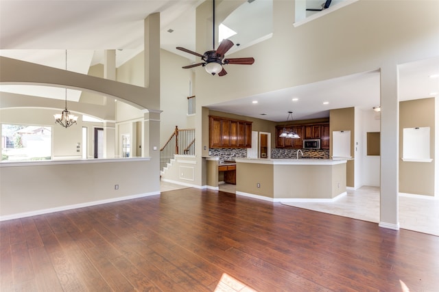 unfurnished living room with wood-type flooring, ceiling fan with notable chandelier, decorative columns, and high vaulted ceiling