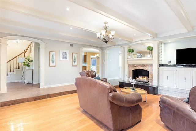 living room with decorative columns, a premium fireplace, light hardwood / wood-style floors, beamed ceiling, and a chandelier