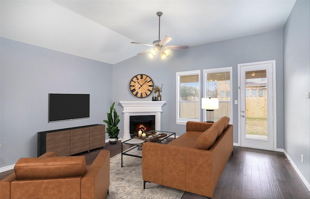 living area with a warm lit fireplace, baseboards, wood finished floors, and a healthy amount of sunlight