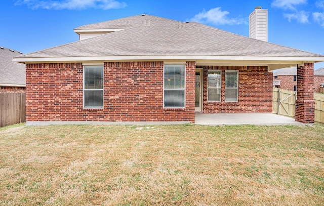 rear view of property featuring roof with shingles, brick siding, fence, and a patio