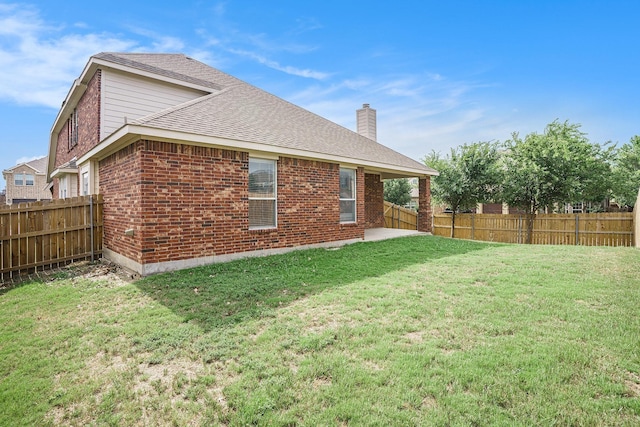 back of house with a yard, a fenced backyard, a chimney, and brick siding