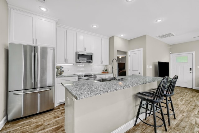 kitchen with stainless steel appliances, a center island with sink, and white cabinetry