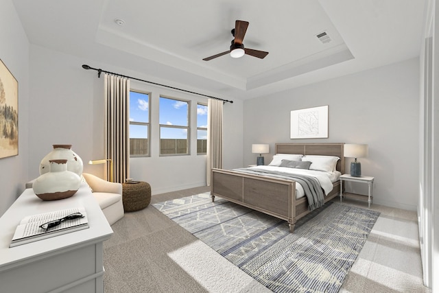 carpeted bedroom with a raised ceiling and ceiling fan