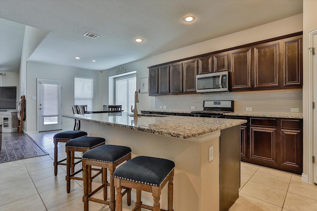 kitchen with black stove, sink, light tile patterned floors, and an island with sink