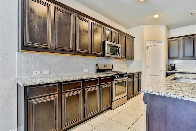 kitchen featuring light tile patterned floors, tasteful backsplash, light stone counters, dark brown cabinetry, and stainless steel appliances