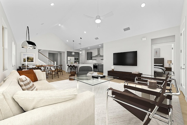 living area featuring high vaulted ceiling, visible vents, a ceiling fan, stairway, and light wood finished floors