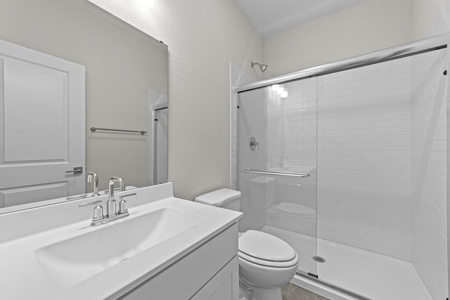 full bath featuring a stall shower, a textured wall, vanity, and toilet