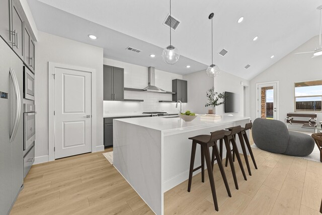 kitchen featuring light wood finished floors, light countertops, visible vents, appliances with stainless steel finishes, and wall chimney exhaust hood