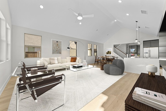 living area with high vaulted ceiling, light wood-type flooring, stairway, and a ceiling fan