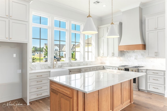 kitchen with a center island, light wood-type flooring, appliances with stainless steel finishes, white cabinetry, and sink