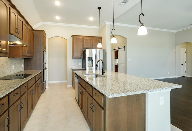 kitchen featuring a center island with sink, a barn door, decorative light fixtures, and stainless steel appliances