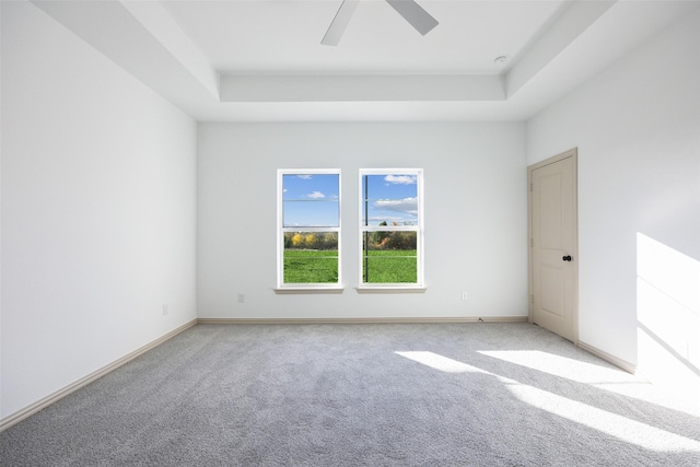 carpeted empty room with a raised ceiling and ceiling fan