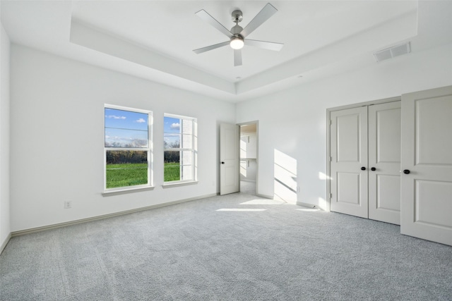 unfurnished bedroom with light colored carpet, ceiling fan, and a tray ceiling