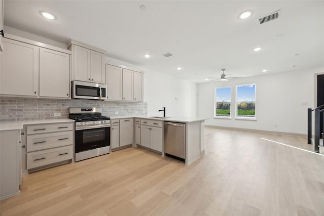 kitchen with sink, ceiling fan, light hardwood / wood-style floors, kitchen peninsula, and stainless steel appliances