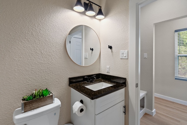 bathroom with baseboards, a textured wall, toilet, wood finished floors, and vanity