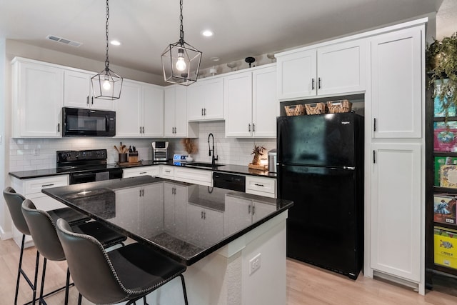 kitchen with visible vents, a kitchen island, a sink, light wood-type flooring, and black appliances