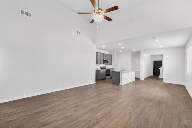 unfurnished living room featuring dark wood-style floors, ceiling fan, visible vents, and baseboards