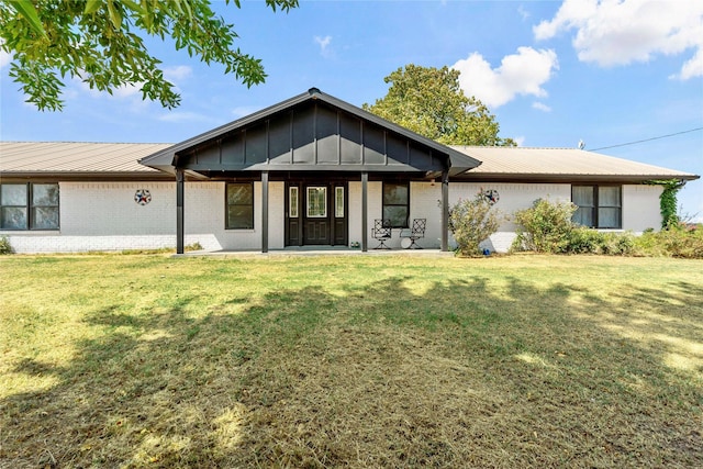 rear view of house featuring board and batten siding, metal roof, a lawn, and brick siding