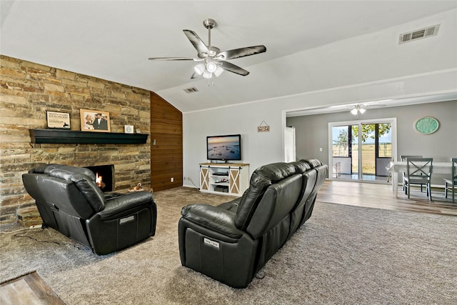 carpeted living area with vaulted ceiling, a stone fireplace, visible vents, and a ceiling fan