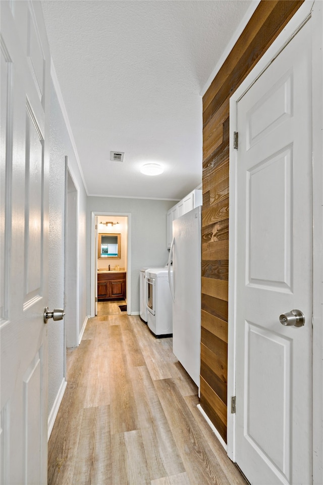 corridor with light wood-type flooring and separate washer and dryer