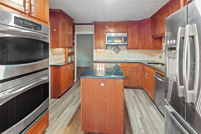 kitchen with light wood-type flooring, a kitchen island, appliances with stainless steel finishes, and a sink