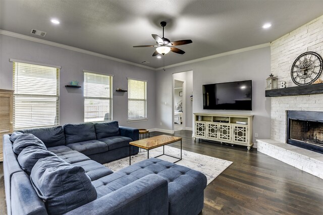 living room with ceiling fan, a stone fireplace, ornamental molding, and dark hardwood / wood-style flooring