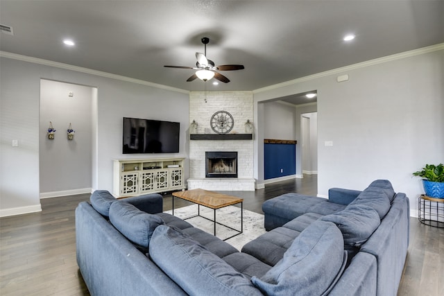 living room with ceiling fan, a large fireplace, crown molding, and hardwood / wood-style flooring