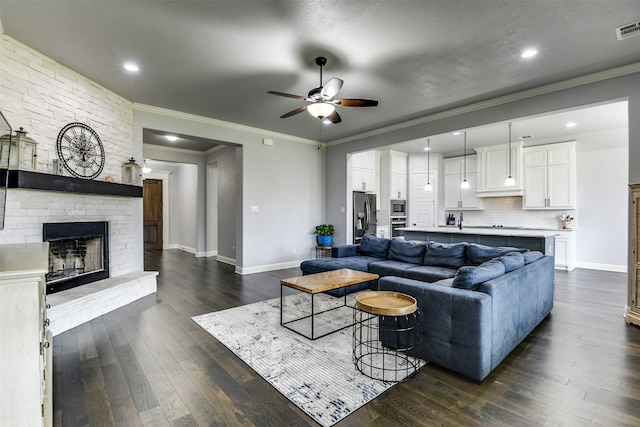 living room with sink, ornamental molding, a brick fireplace, dark wood-type flooring, and ceiling fan