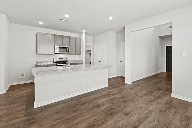 kitchen featuring light stone counters, a center island with sink, appliances with stainless steel finishes, and gray cabinets