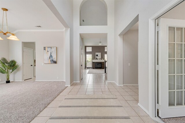 foyer with ornamental molding, a fireplace, light colored carpet, and ceiling fan