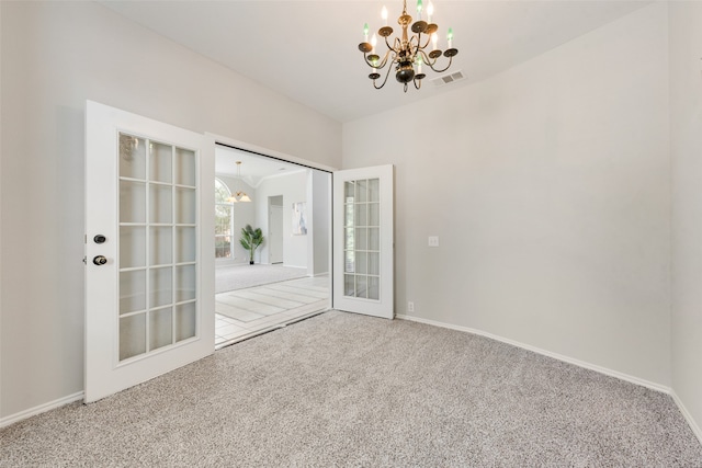 carpeted spare room featuring french doors and an inviting chandelier