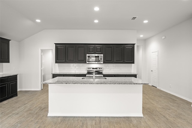 kitchen with light stone counters, stainless steel appliances, and a center island with sink