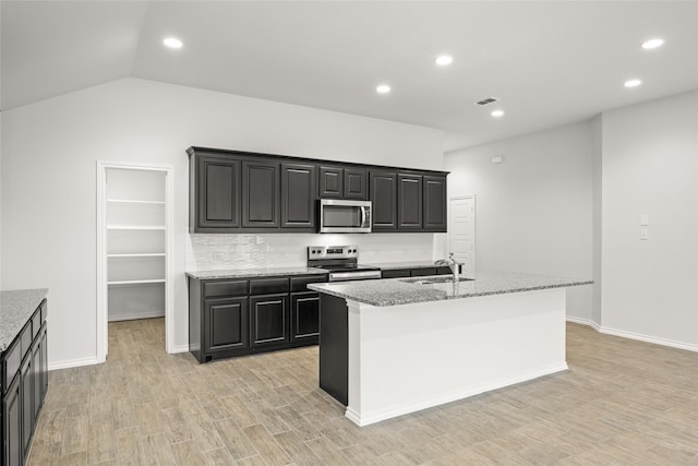 kitchen with light hardwood / wood-style flooring, a kitchen island with sink, backsplash, stainless steel appliances, and light stone counters