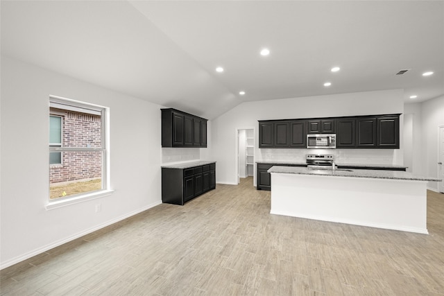 kitchen with a center island with sink, light hardwood / wood-style flooring, stainless steel appliances, light stone countertops, and decorative backsplash