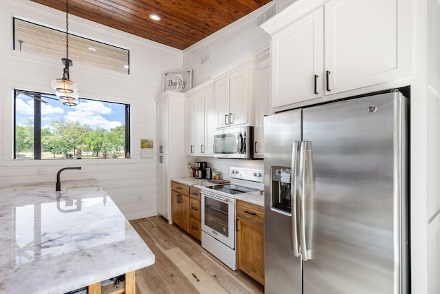 kitchen with sink, stainless steel appliances, white cabinets, hanging light fixtures, and light stone countertops