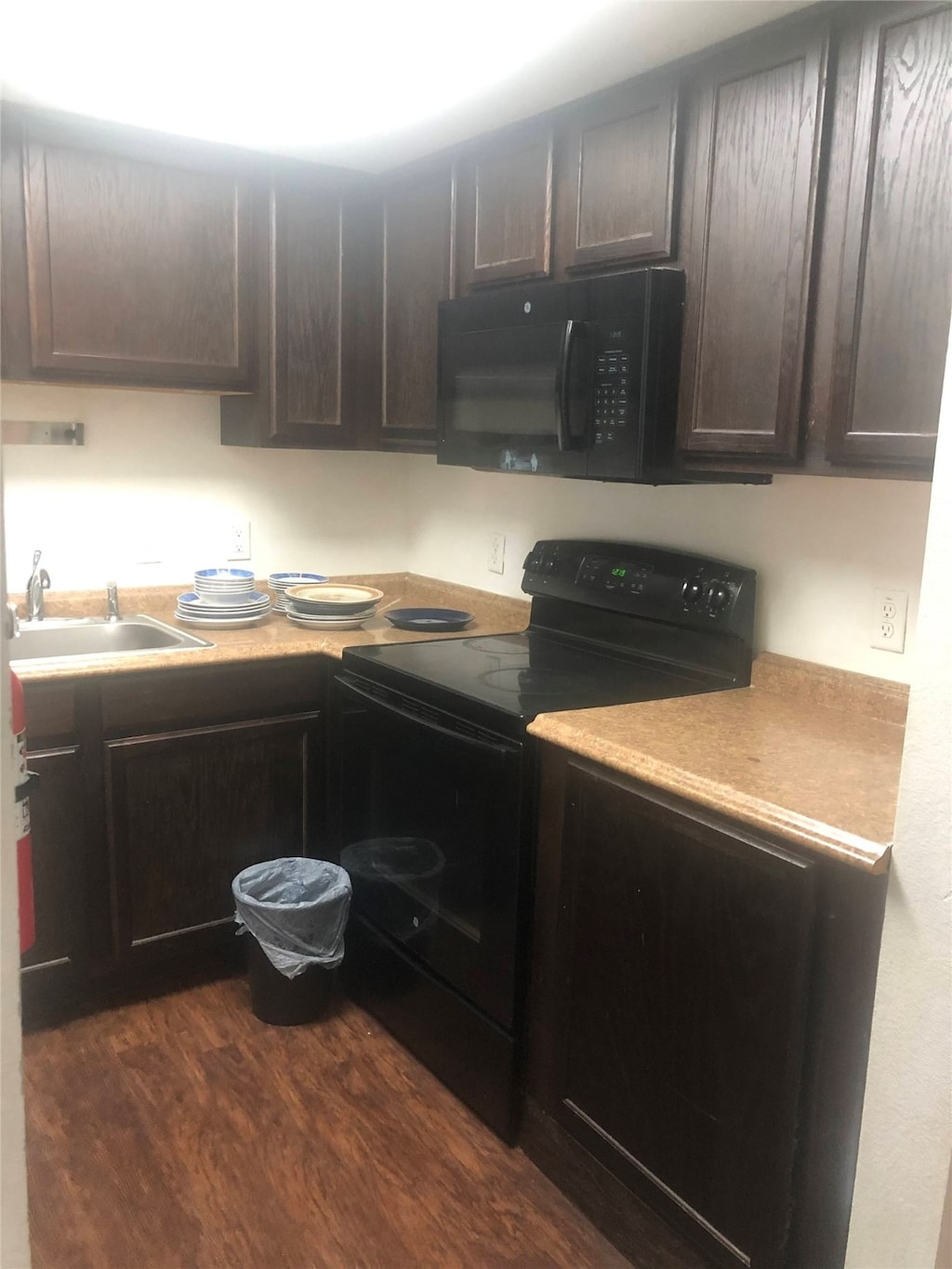 kitchen with sink, dark brown cabinets, dark hardwood / wood-style flooring, and black appliances