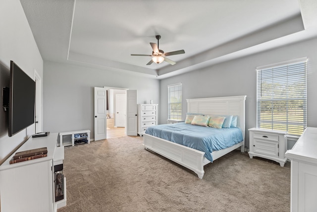 bedroom featuring a tray ceiling, ceiling fan, connected bathroom, and light carpet