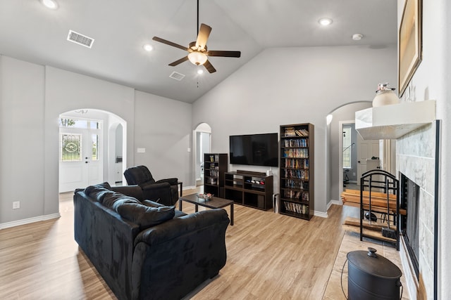 living room with ceiling fan, high vaulted ceiling, light hardwood / wood-style floors, and a tile fireplace