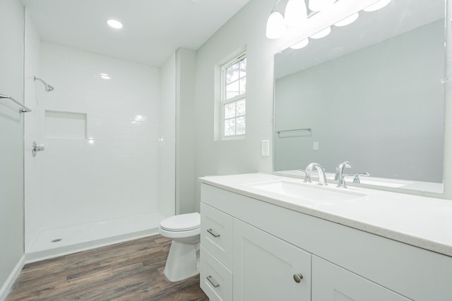 bathroom with hardwood / wood-style floors, toilet, a tile shower, and vanity