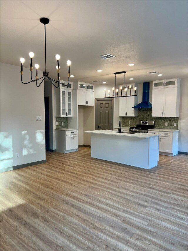 kitchen featuring a center island with sink, white cabinetry, gas stove, and wall chimney exhaust hood