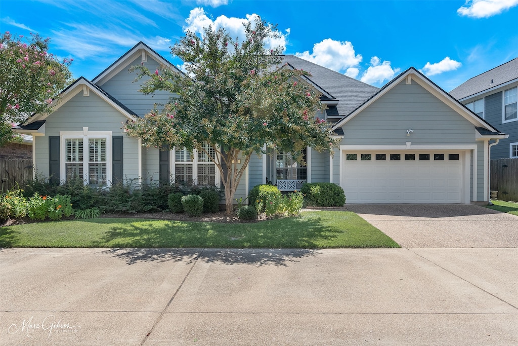 view of front of house with a garage, a shingled roof, concrete driveway, fence, and a front lawn